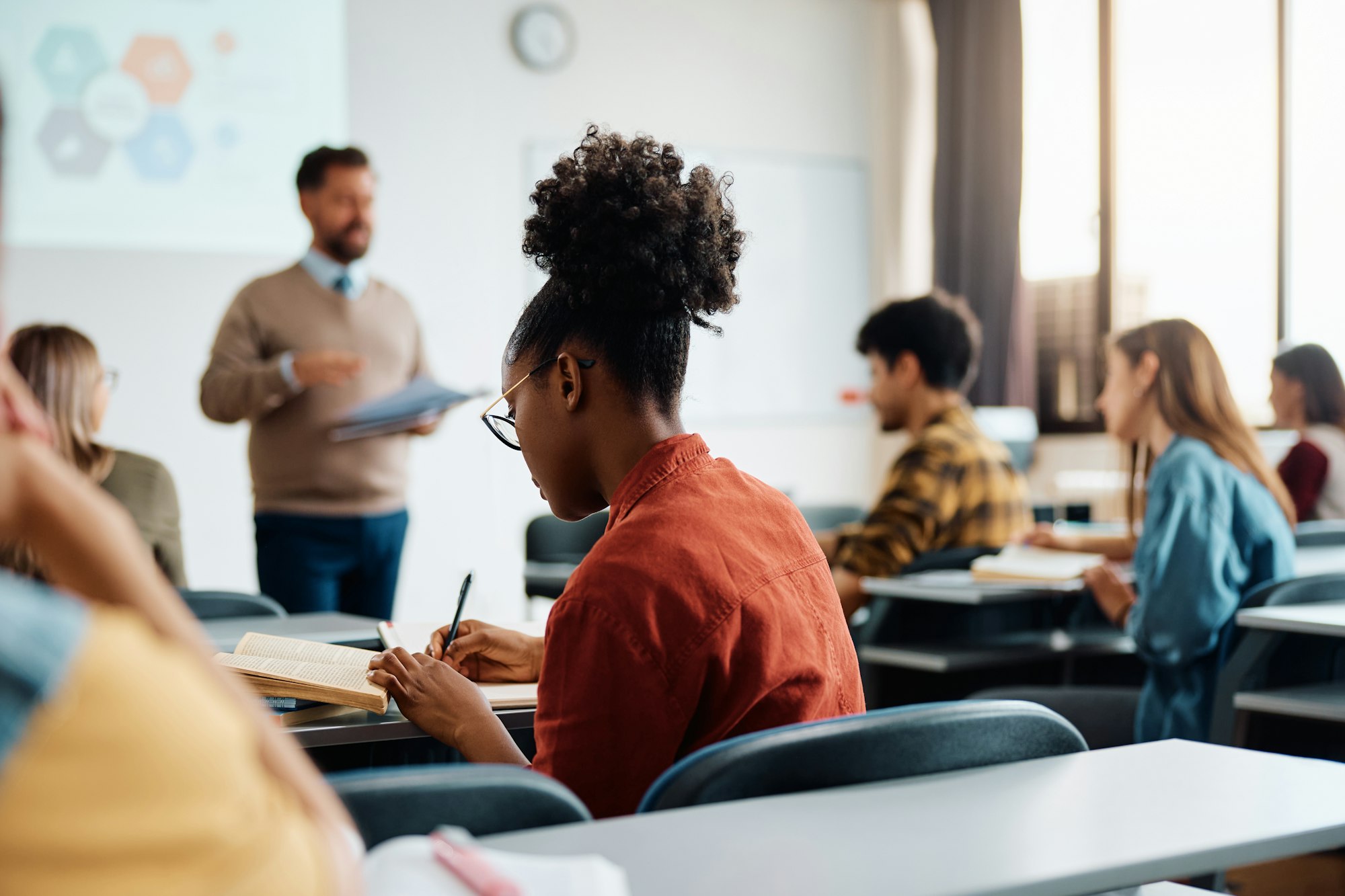 Black female student taking notes during a class in lecture hall.